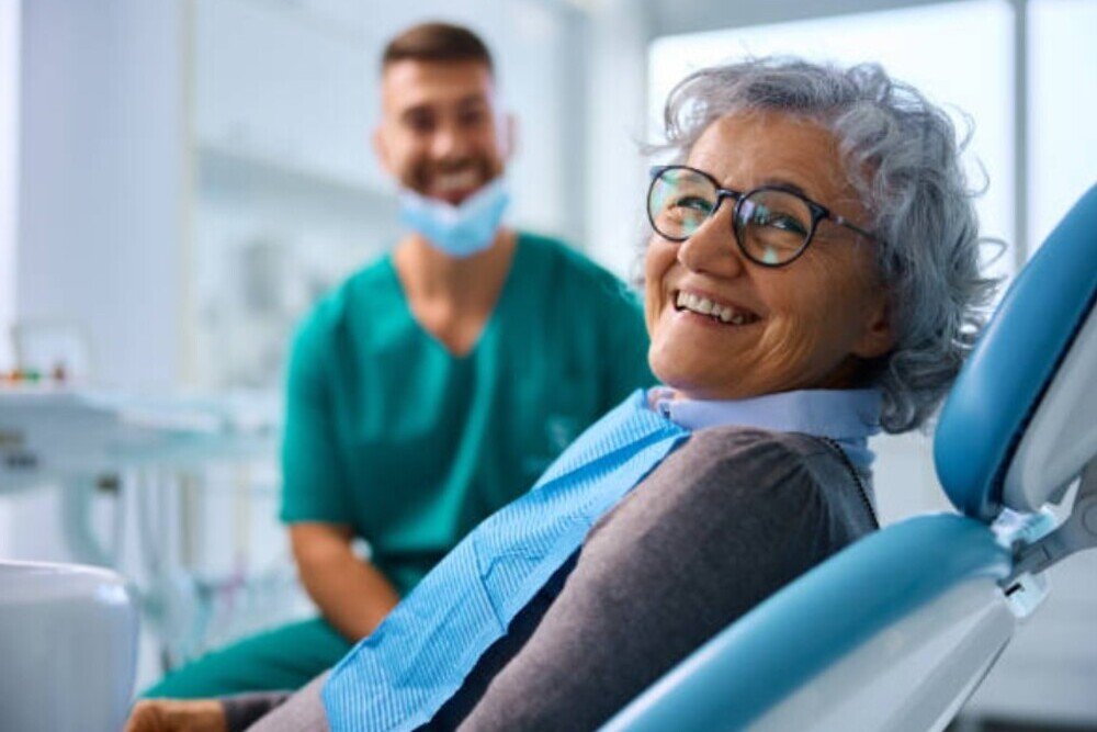 paciente mayor sonriendo en clinica dental con dentista de fondo en fuencarral